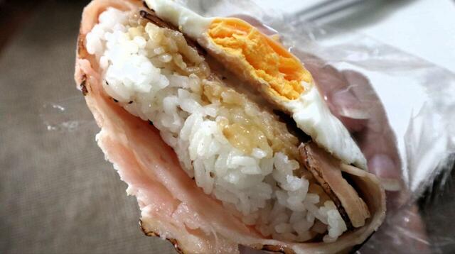 【トライアル あぶりベーコンエッグおにぎり】目玉焼きの下に、醤油ベースのたれが塗られたふっくらご飯が現れます