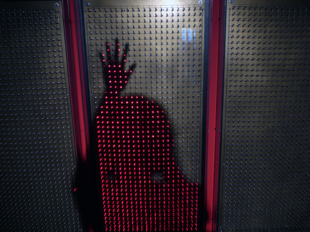 『レイヨ＝グラフィー』森脇裕之／光センサと発光ダイオードが一組になったパーツがパネルに並んで画面を構成。観客の影にあわせて「影絵」のように赤い光が点灯し、影が主役のような存在感を放ちます。