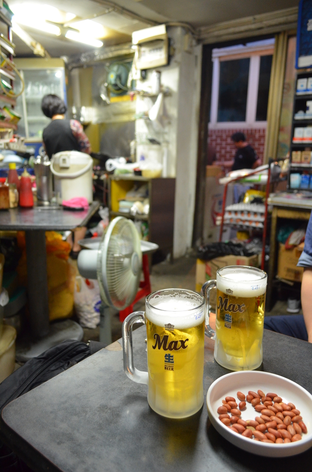『ソウル食品』では、酒だけ飲んでもピーナッツなどの乾きものが添えられる。奥はマドンナ（女将）の後ろ姿。店は22時までだが、注文は21時までに