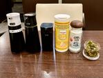 【トーキョーアジフライ】各テーブルやカウンターに用意された調味料。黄色い筒が粉チーズ。右が今月の薬味、青唐辛子の醤油漬け