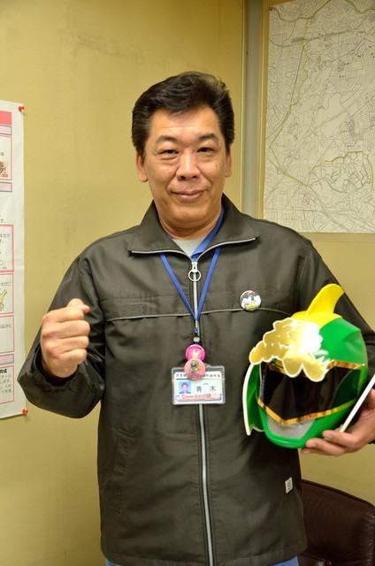 資源循環局緑事務所で副所長を務める青木雅徳さん。グリーンのマスクを持ってポーズ
