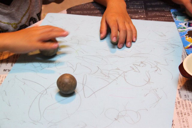 30分置いた後のだんごを表面がツルツルした下敷き（芯をつくった時に洗っておいたもの）の上で軽く転がします。※ちなみに作業する台の表面は、定期的に土などを取り除いて、綺麗にしておきましょう。