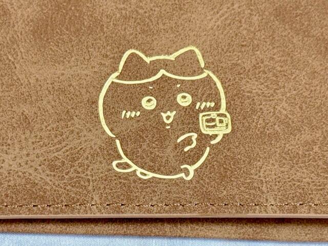 フロントには、ハチワレのイラストがゴールドの箔押しでデザイン。草むしり検定証を見せているイラストで、草むしり検定編のエピソードを思い出してしまう胸アツすぎるチョイス♪【アベイル×ちいかわ】「カードケース（ハチワレ）」