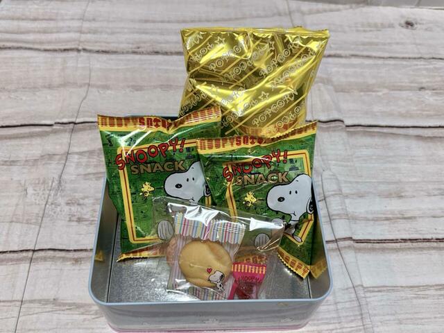 お菓子の内容は、スナック菓子10g×2袋、スヌーピー型焼菓子×1個、スヌーピー柄焼菓子5g×1個、ポップコーン12g×1袋、キャンディ（ストロベリー風味）3g×1個））
