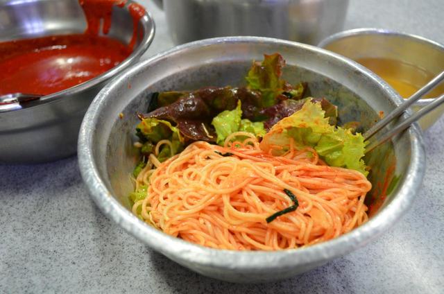 ピビムミョンはそのままでもじゅうぶん辛いのだが、釜山の専門店ではさらに辛く食べたい客ために激辛ソース（左上）を用意している