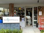 【Blue Poppy Bakery(ブルーポピーベーカリー)】)外観。店の看板の裏側にテラス席があり、コーヒーなども頼める