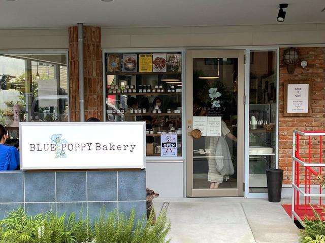 【Blue Poppy Bakery（ブルーポピーベーカリー）】）外観。店の看板の裏側にテラス席があり、コーヒーなども頼める