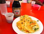 【台湾食べ歩きの旅 #11】廟脇の朝市の一角に円卓が置かれ、卵焼きと保力達（パオリータ）が並んでいる。養命酒をもっと甘く濃くしたような栄養ドリンク