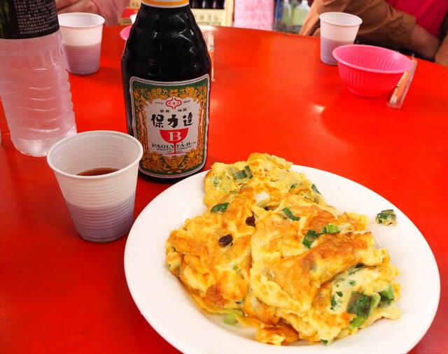 【台湾食べ歩きの旅 #11】廟脇の朝市の一角に円卓が置かれ、卵焼きと保力達（パオリータ）が並んでいる。養命酒をもっと甘く濃くしたような栄養ドリンク