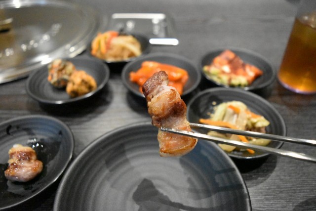 よく焼いた豚肉をキムチや野菜に巻いて食べる