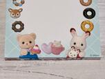 【シルバニアファミリー メモ帳（ドーナツ）】下部には、ショコラうさぎの赤ちゃん クレムと、クマの赤ちゃん ジェイソンがドーナツを持っているアートプリント入り