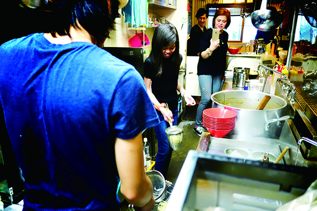 ラーメン体験のプロセス1：湯切り／職人のデモンストレーションを見学したら、いざ実践！ラーメン作りに欠かせない湯切りに挑戦する。ザルの持ち方や、湯切りのコツを学ぶ。