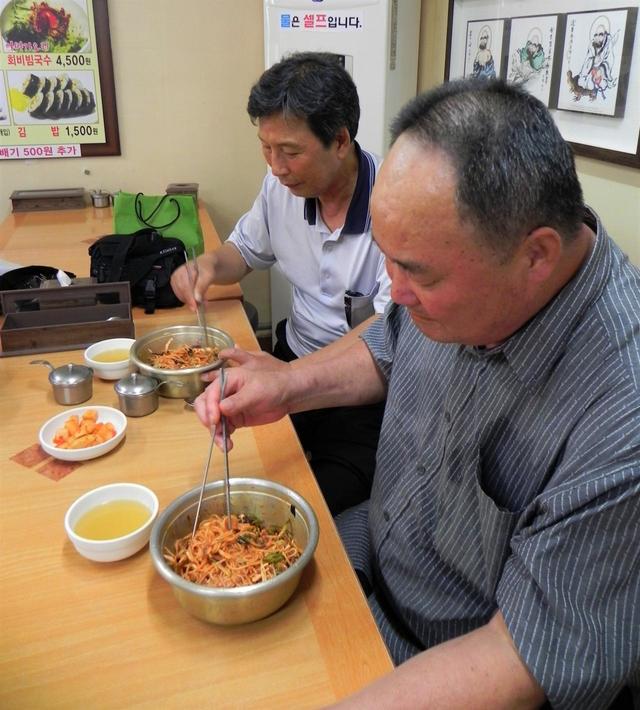 顔を真っ赤にして嬉々としてピビムミョンを食べる中高年。ここ数年、ピビムミョンの対角線上にある淡白な平壌冷麺（そば粉のスープ麺）が人気だが、辛くて濃厚なピビムミョンでないと食べた気がしないいう韓国人は多い