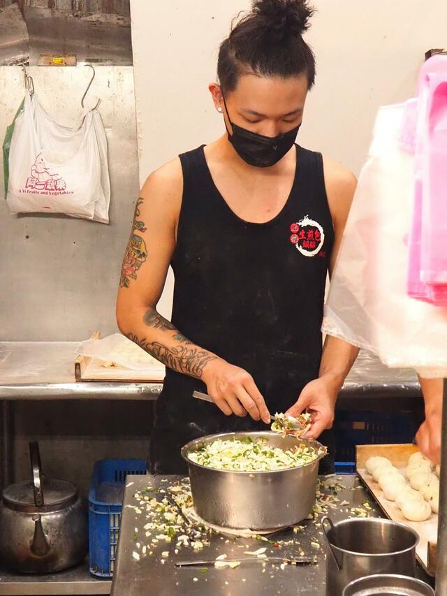 【台湾6泊7日食べ歩きの旅①台北編】屋台の奥でまんじゅうの餡を器用に皮で包んでいく若者。タンクトップからむき出しの腕には流行りのタトゥーが見える