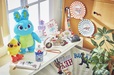 左から) ぬいぐるみ  1,800 円/ぬいぐるみ  2,500 円/ウォレット 3,500 円/マグカップ 1,800 円/ピアス&ピアススタンド 3,300 円/ショルダーバッグ 3,900 円/ポーチ 1,900 円/カメラストラッ プ 2,000 円/プレート(4 枚セッ ト) 2,000 円/かさ 2,500 円