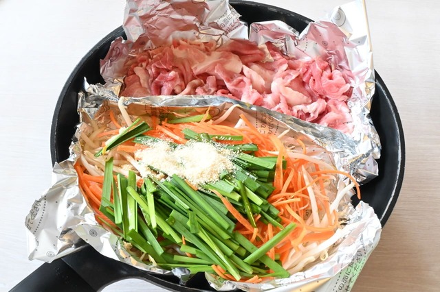 【ワンパン！石焼風ビビンバ】フライパンにフライパン用のアルミホイルを2枚、中央で仕切るようにしき、一方にもやし、にんじん、にらをのせ、調味料をかけます