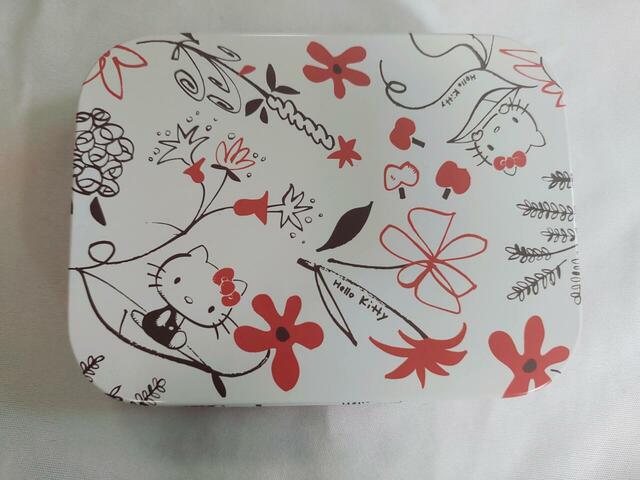 【ハローキティの缶ケース】白い背景に赤・茶色で描かれたキティとお花のイラストつき