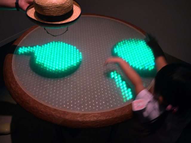 『Tea for Angel（ティー・フォー・エンジェル）』森脇裕之／一見普通のテーブルに手をかざすと、そこにできた影が緑色に光り輝く。テーブルは子供も手に届く高さなので、手や腕だけでなく、帽子など色々な影を映して楽しんでいました。