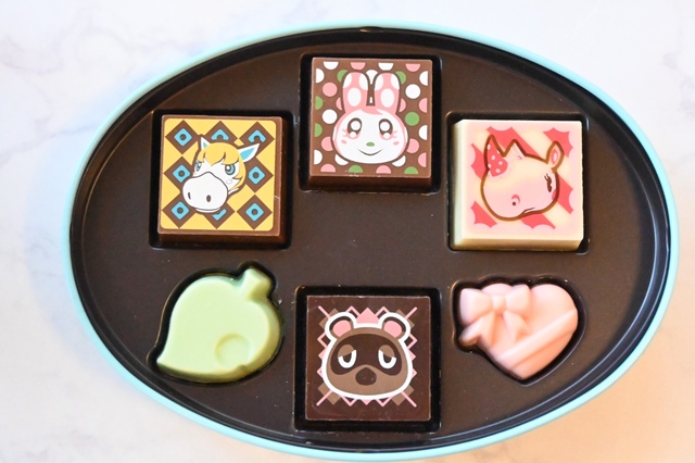 【ゴディバ meets どうぶつの森 アソートメント/Blue 6粒入 フタ付きティーマグカップセット】ブルーの缶には、たぬきち、アンソニー、クリスチーヌ、パティ、葉っぱのマーク、ハートのチョコレート（ピンク）の6粒のチョコ入り。